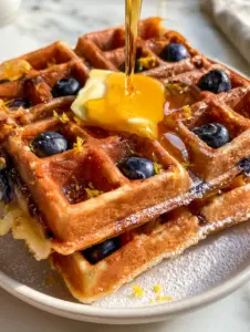 Handheld photo of Belgian blueberry waffles showing the deep golden ridges and indigo blueberries tucked into pockets. (blueberry waffles)