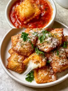 Top-down view of a single air fryer ravioli being dipped into a ceramic bowl of vibrant red chunky marinara sauce.