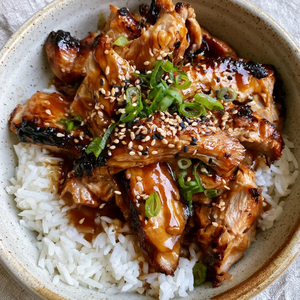 Detail shot of the translucent, dark mahogany-colored glossy teriyaki glaze on pork fibers with sesame seed garnish.