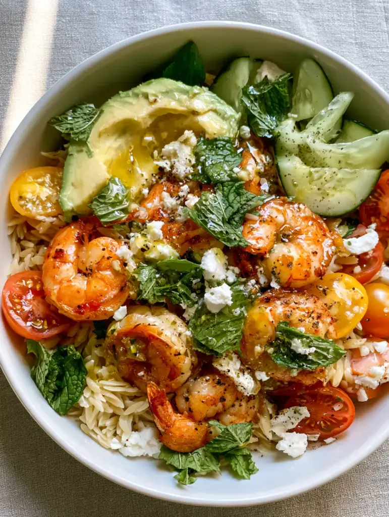 Close up of golden-seared jumbo shrimp and blistered tomatoes on a bed of orzo pasta.